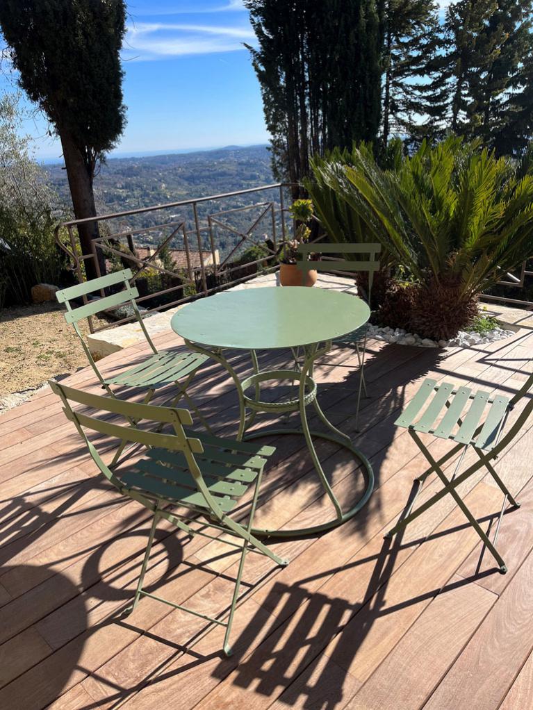 terrasse en bois exotique aménagée d'une table et chaisse en fer forgé vert olive